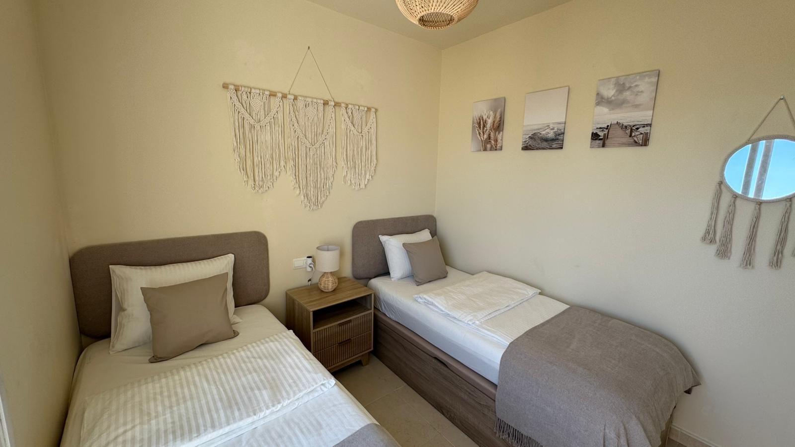 Twin bedroom seen from the corner, with wall art and mirror